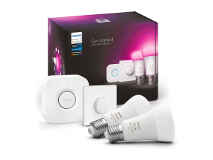 A product image of a Philips Hue Starter Kit. It shows a large black box with product imagery on the front. In front of the box are its contents. These include two bulbs, a dimmer knob, and a bridge.