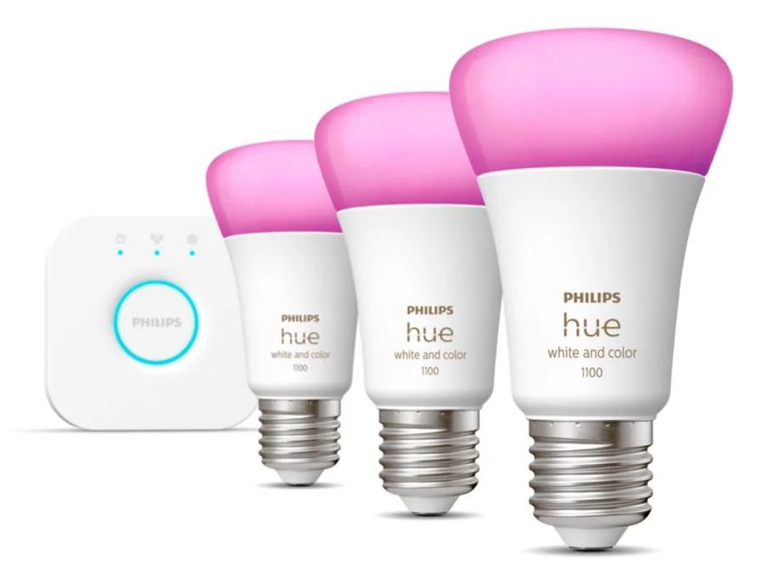 A product image of three Philips Hue bulbs and a Hue Bridge. The bulbs are lined up on an angle receding from the viewer and to the left, towards the bridge in the background. The bulbs are mostly white, lit up in a purple colour. The bridge is white with a lit up blue ring.