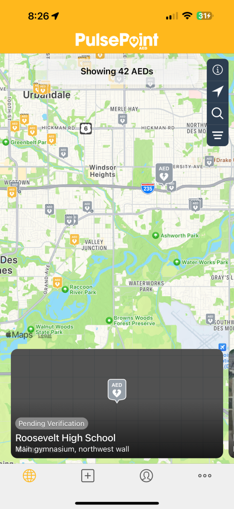 A screenshot of the PulsePoint mobile app displaying a map of the Urbandale area, with icons indicating the locations of 42 Automated External Defibrillators (AEDs). A detailed popup is visible for one specific AED at Roosevelt High School, noting it is on the northwest wall of the main gymnasium and is pending verification.