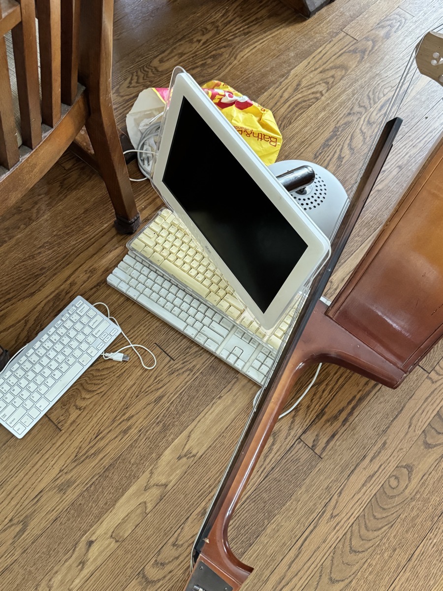 Attic pixar lamp imac sitting on the floor viewed from above with 3 old keyboards, and oddly a cello.