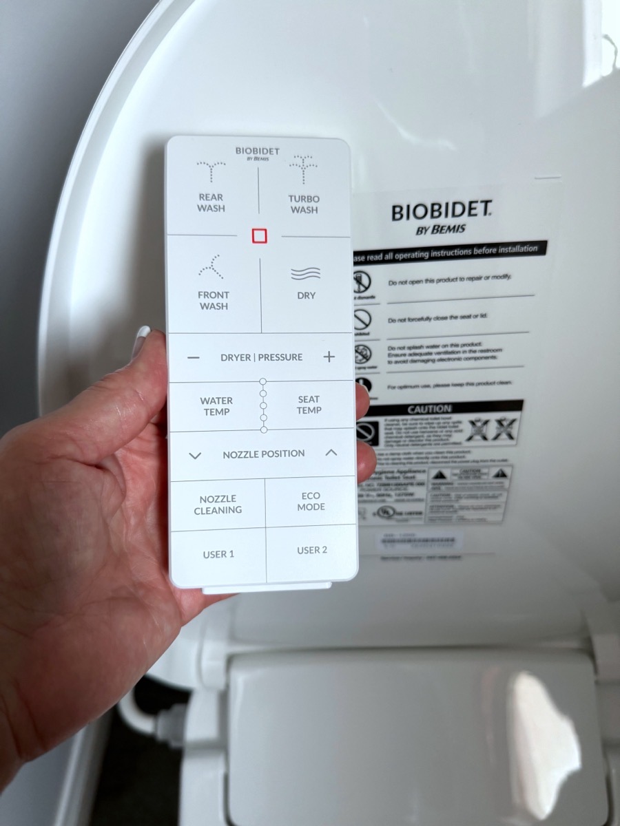 BioBidet remote infront of bidet seat. Held in a woman&#39;s hand to show scale.