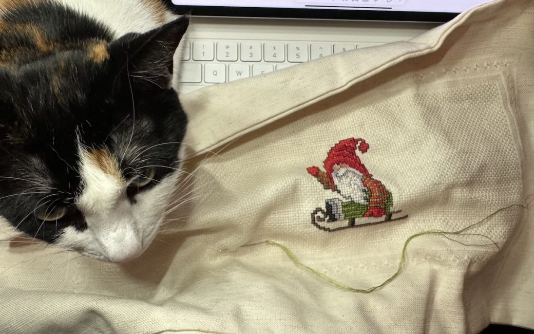 calico on my lap while cross stitching Christmas gnome with iPad in the background showing the pattern