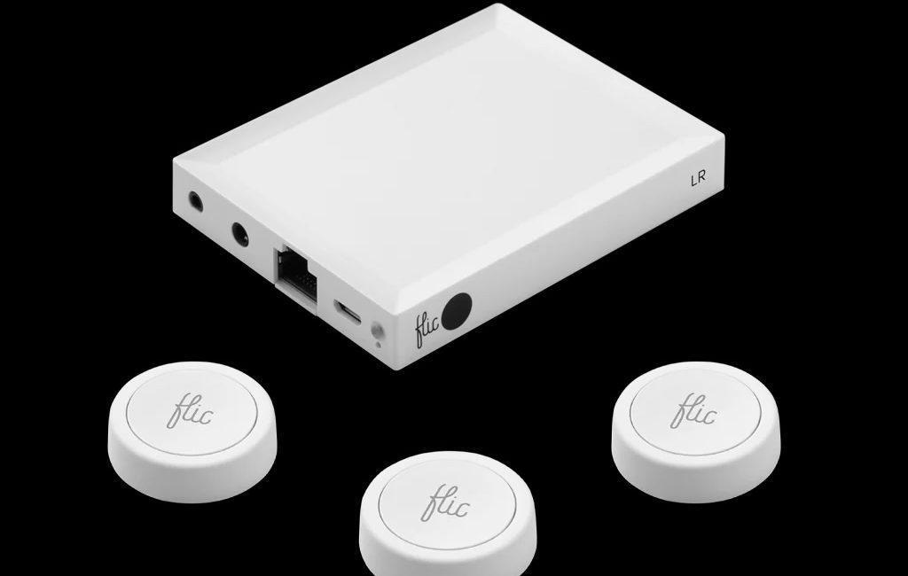 Three Flic Buttons are shown around a Flic Hub, all white in color with the Flic logo embossed on them. The buttons are circular and about an 1" in diameter and 1/4" thick. The Flic Hub is a rectangular plastic device with a micro and Ethernet ports, an IR Receiver window, and a 1/4” audio jack input on one side. It measures about 3-1/2” x 2-1/2” x 1/2”.